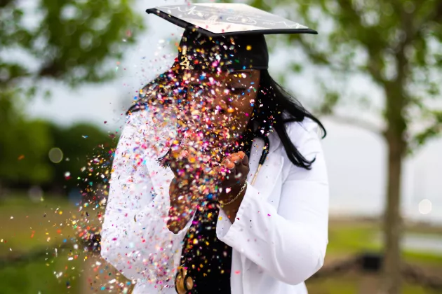 Student som tagit examen blåser konfetti. Foto.