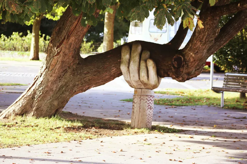 Skulpturhand håller upp en stor gren. Foto.