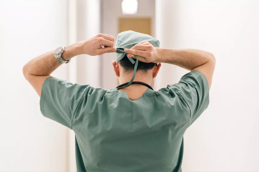 Kirurg knyter huvudbonad inför operation. Foto.