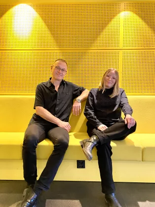 Martin Garwicz och Katarina Bernhardsson är svartklädda framför gul vägg. Foto. 
